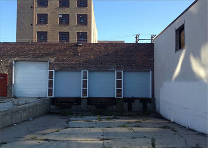 Original still photograph of an empty loading yard with closed shutters in front of a brick building